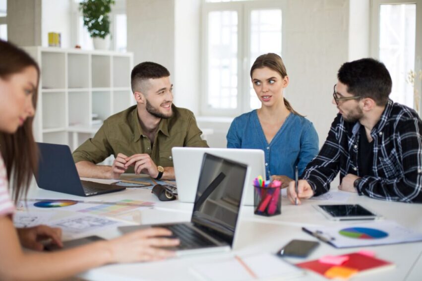 young-creative-people-with-laptop-notepad-working-modern-office-cool-guys-discussing-new-project-together-while-spending-time-work